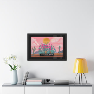 A framed art print featuring a retro-style of a vintage travel poster of a desert illustration with pink sky, yellow sun, and a cluster of prickly pear cactus with pink flowers, displayed on a white wall above a console table with books, a vase of white flowers, and a yellow lamp.