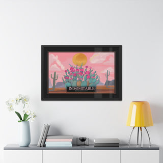 A framed art print featuring a retro-style of a vintage travel poster of a desert illustration with pink sky, yellow sun, and a cluster of prickly pear cactus with pink flowers, displayed on a white wall above a console table with books, a vase of white flowers, and a yellow lamp.